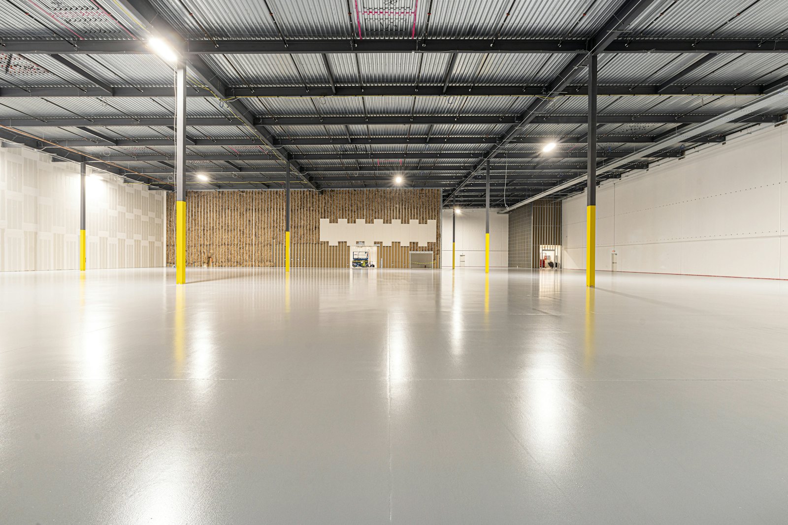 Empty new warehouse with a glossy light-grey concrete floor, steel roof structure and yellow column guards