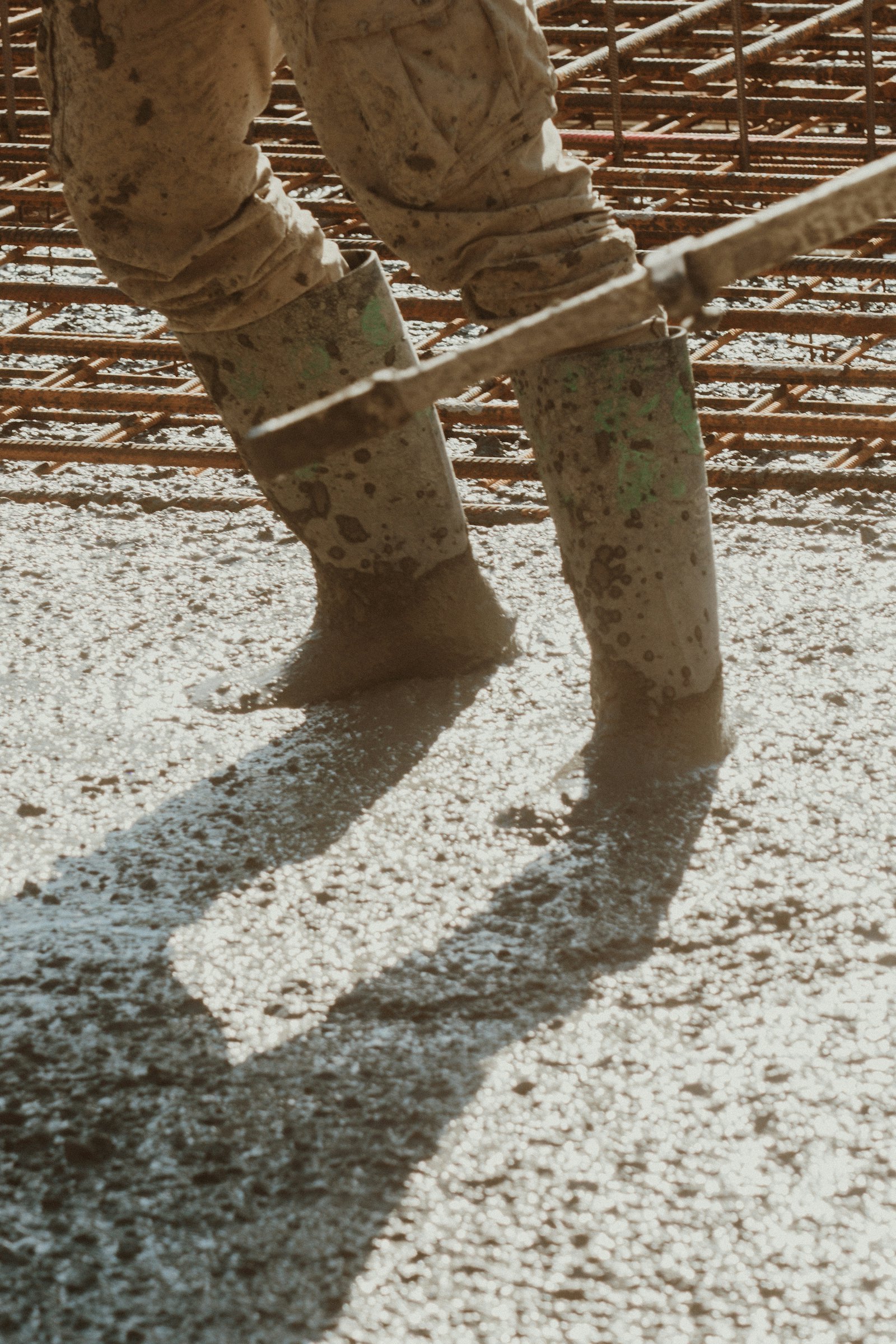 Rubber boots wading through freshly placed concrete over rebar (no face)