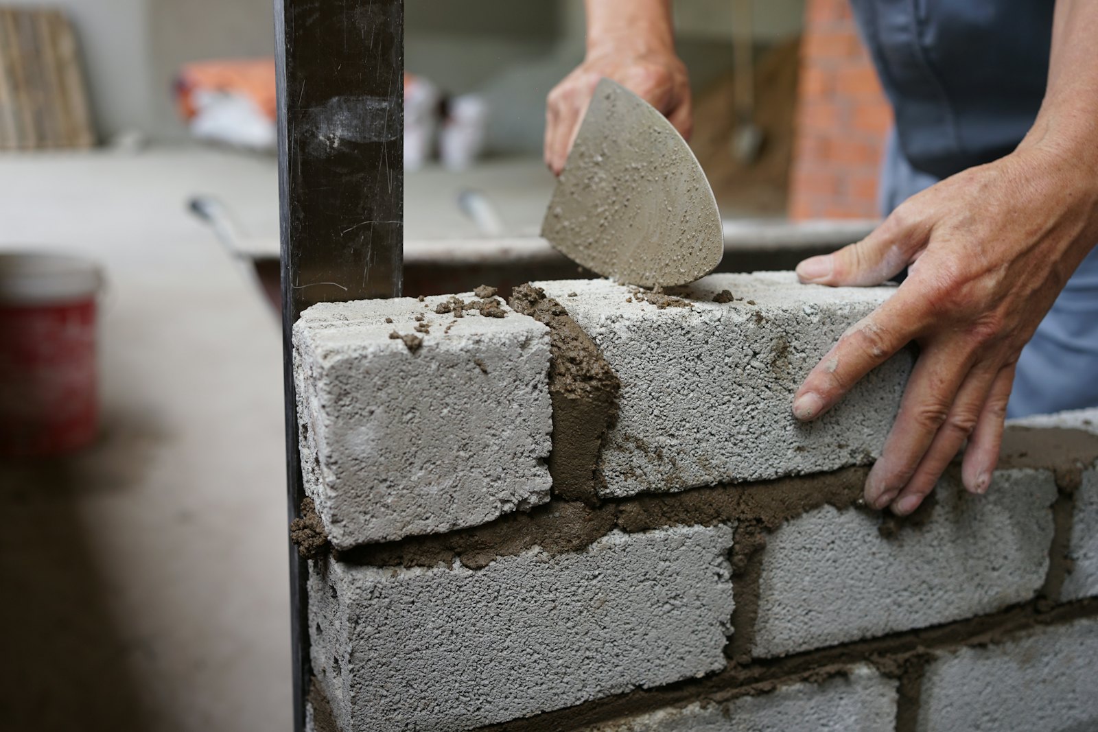 Hands setting a concrete block onto fresh mortar with a pointed trowel